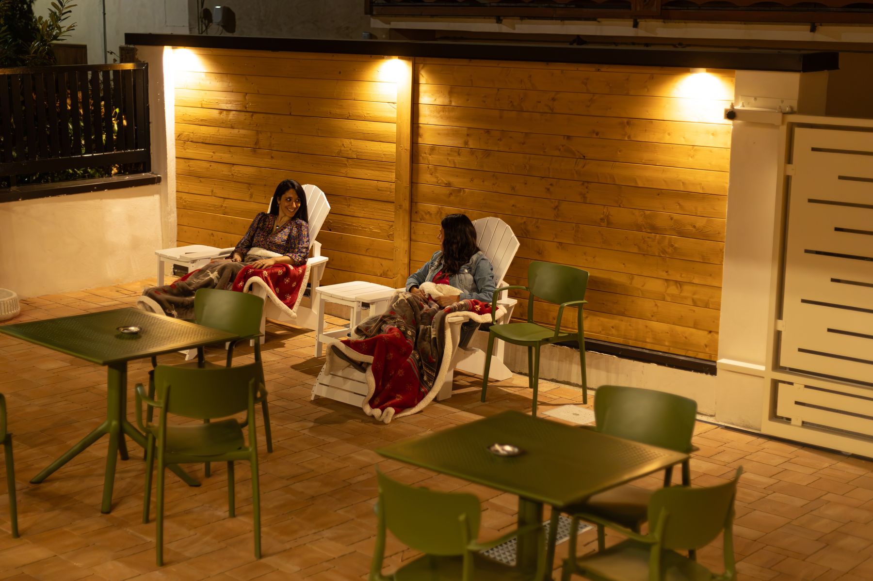 Due ospiti sulle sdraio bianche del dehors, coperte dai plaid, sotto le luci sul legno