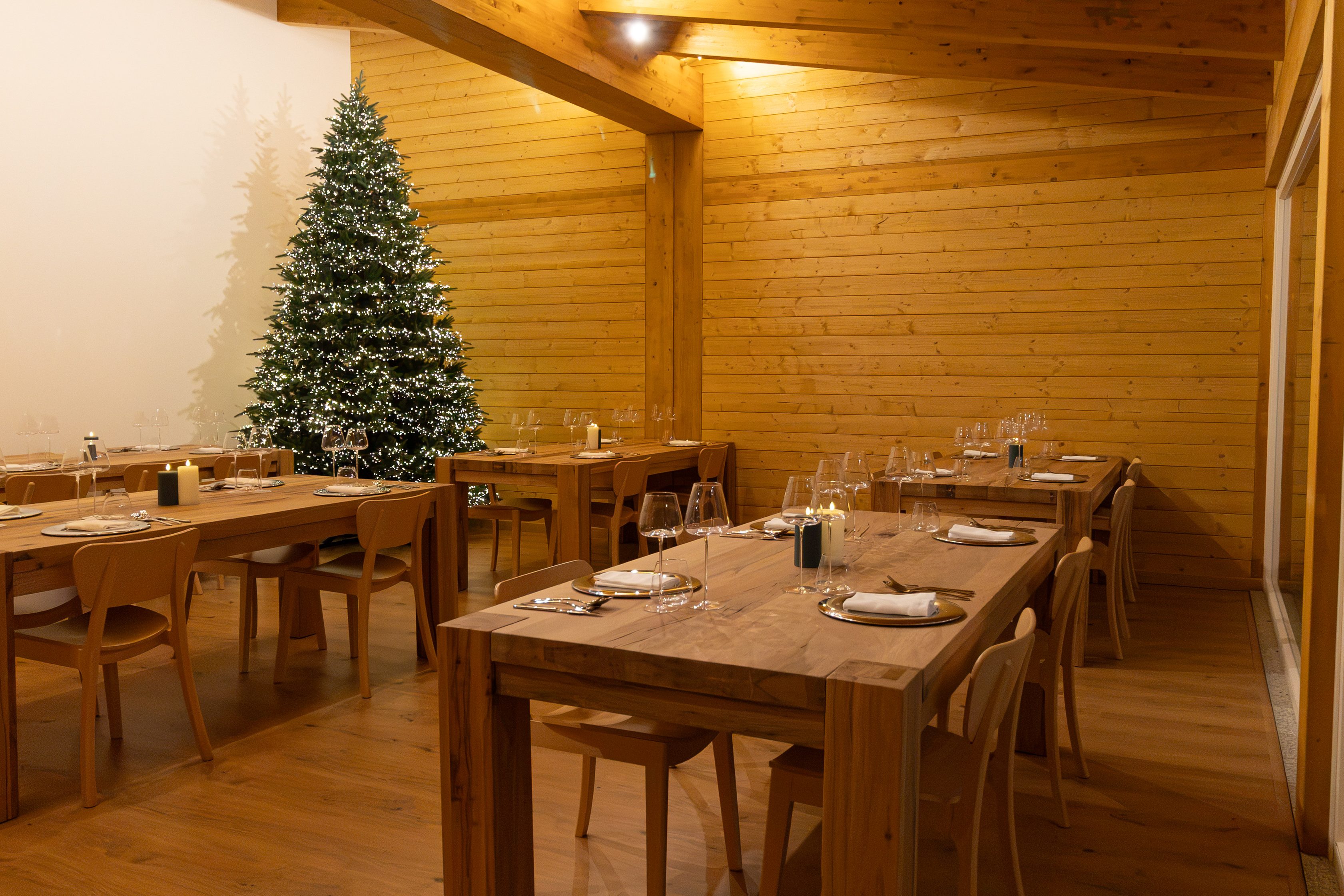 La sala del ristorante con i tavoli in legno apparecchiati e l'albero di Natale acceso
