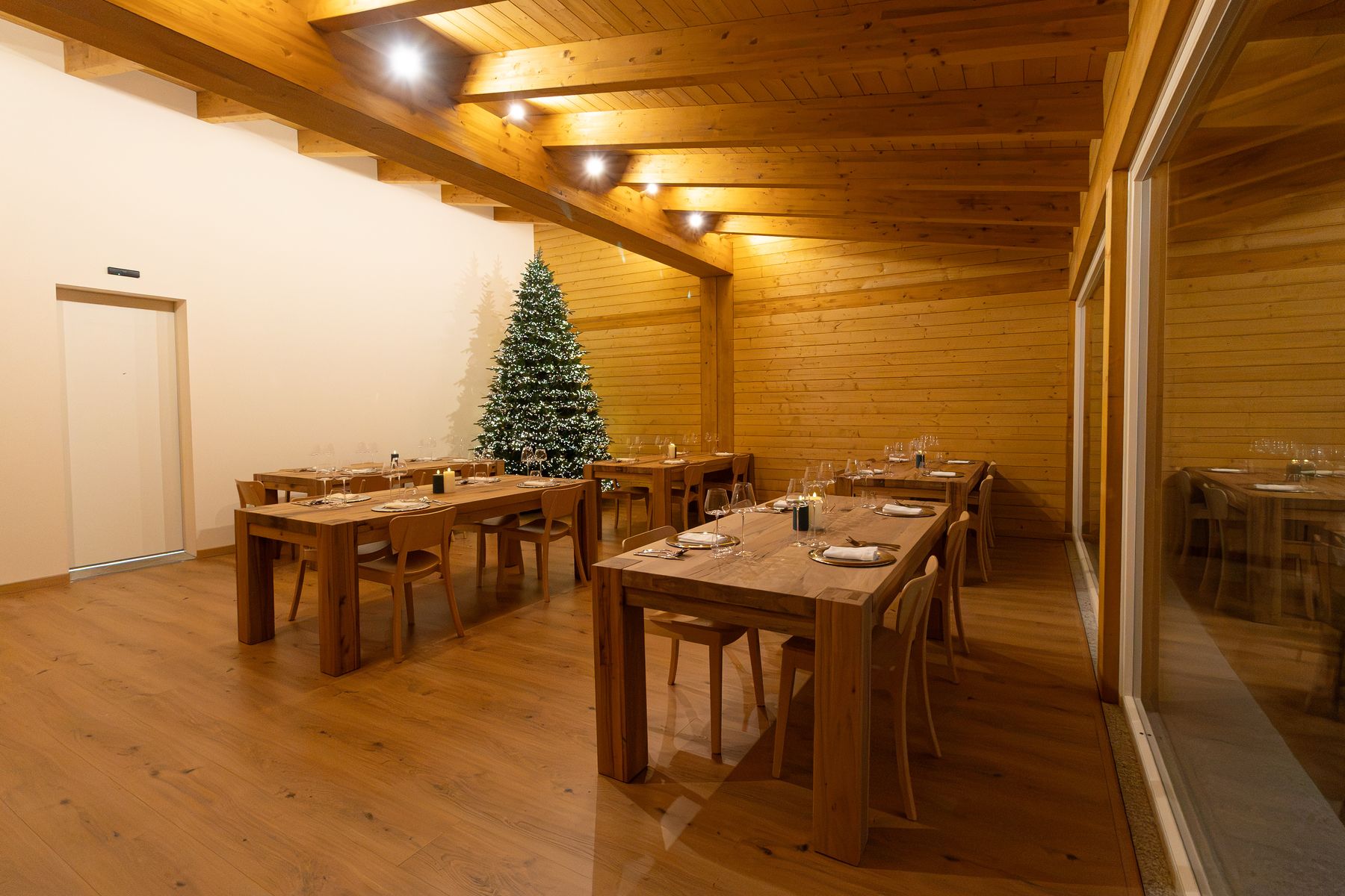 La sala con i tavoli in legno, l'albero in fondo e le vetrate